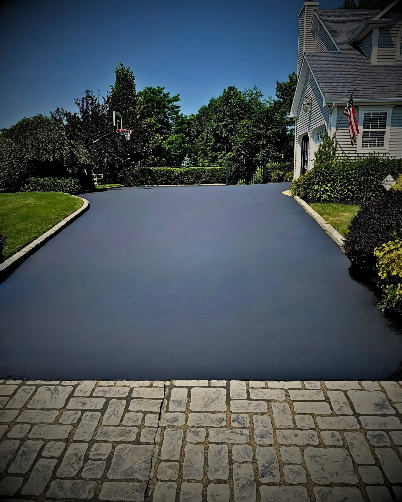 Jet-black freshly sealcoated driveway beside stone pavers